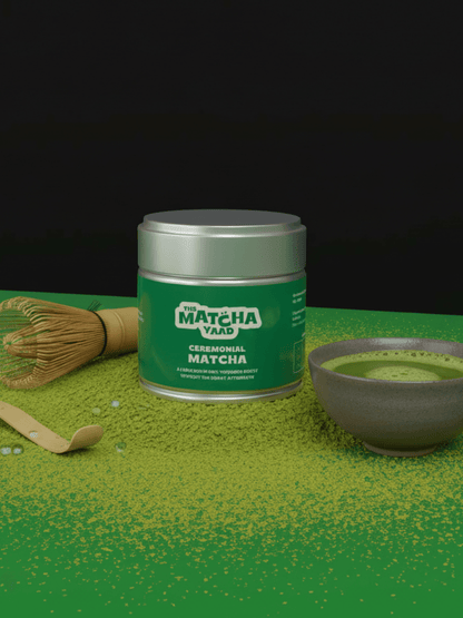 Gokou Ceremonial Matcha tin with bamboo whisk, scoop, and matcha bowl on green powder background, showcasing premium umami-rich tea.