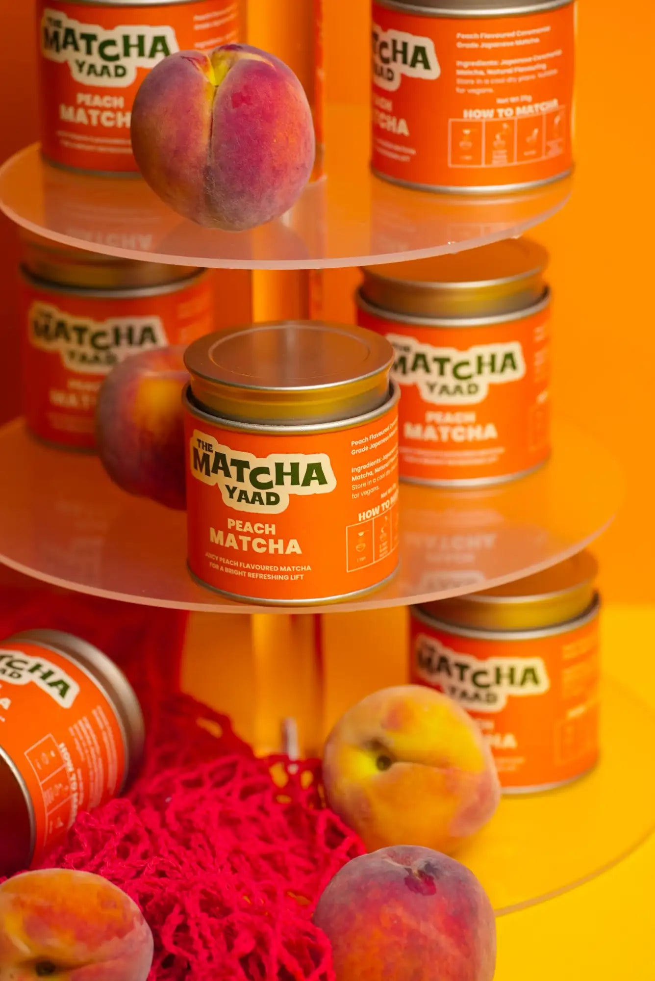 Orange-labeled ’the matcha yaad’ peach matcha tea cans with gold lids, arranged on a tiered stand.