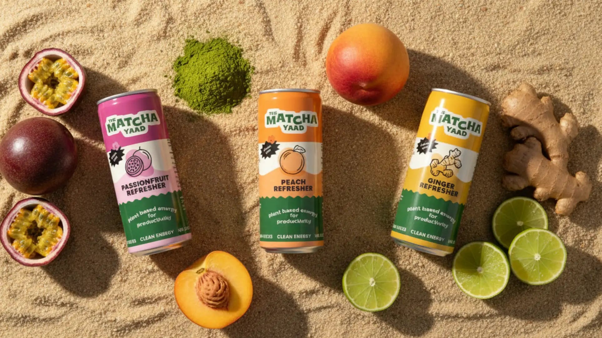 Three cans of Matcha Yaad drinks on sand with fruits and herbs