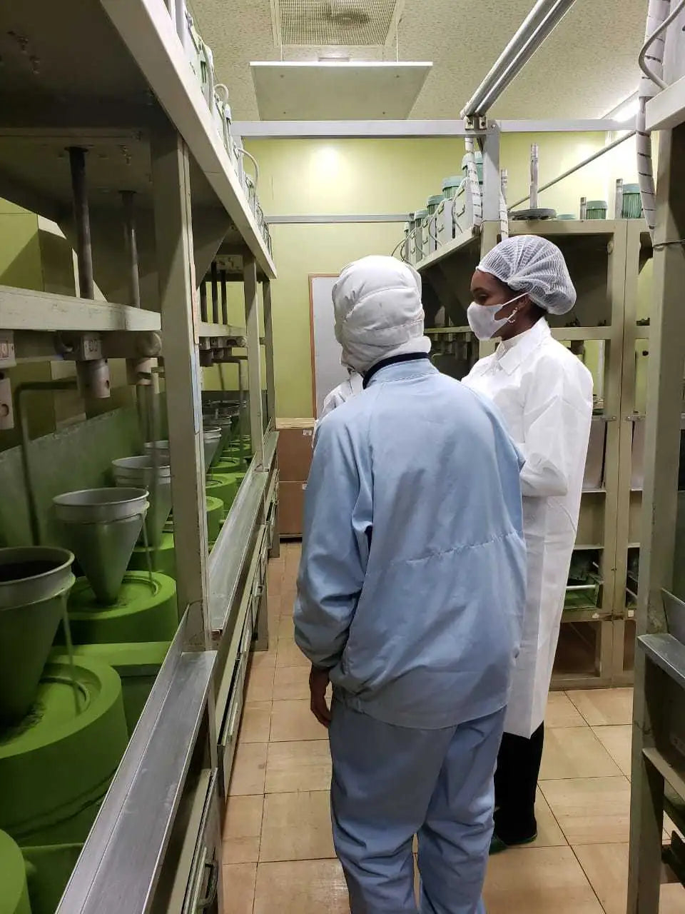 Two individuals in protective lab attire, one wearing a light blue jumpsuit and the other in white with a face mask.