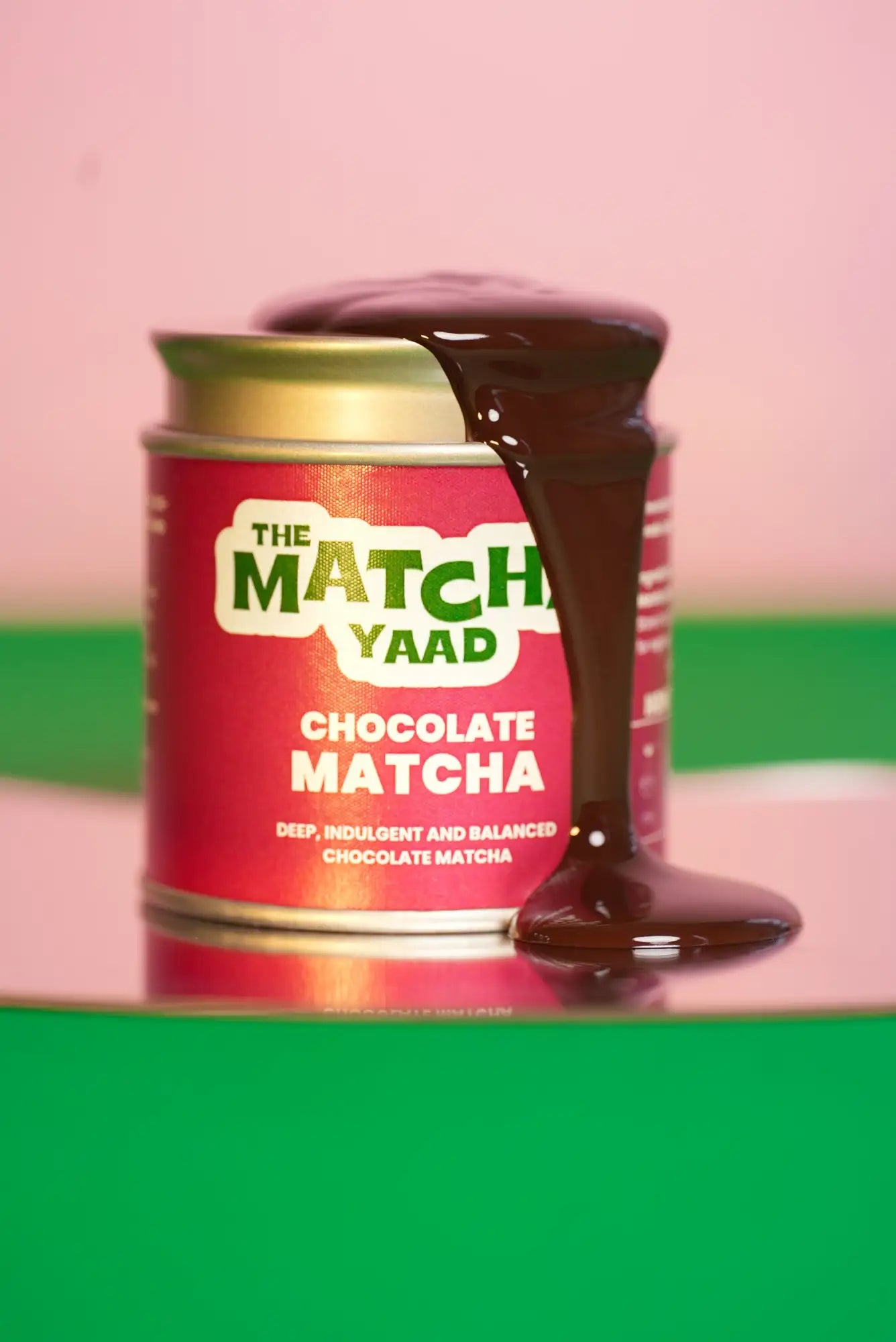 A vibrant red cylindrical tin of the match yaad chocolate matcha, featuring a gold lid and bold green lettering on its label.